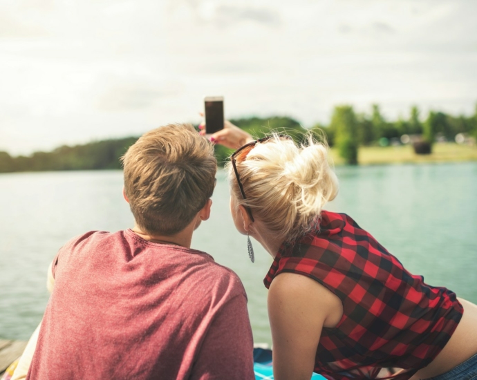 woman and woman sitting on dock both holding one smartphone