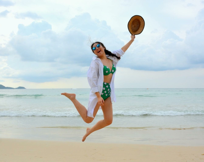 Woman Jumping on Seashore and Holding Hat