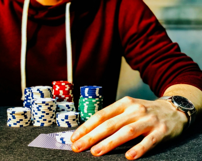 person holding playing cards beside poker chips