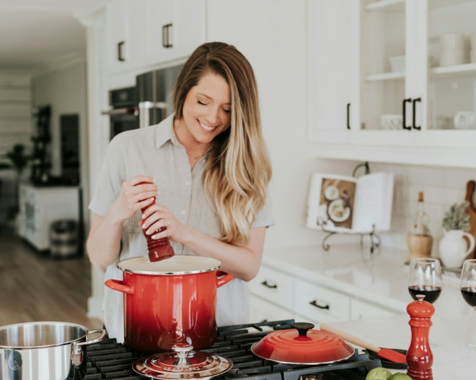 smiling woman standing and putting pepper on stock pot