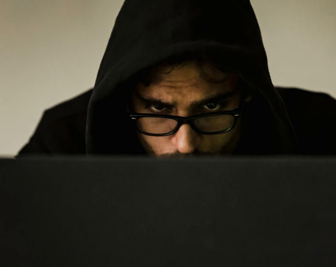 Serious young male programmer wearing black hoodie browsing netbook and hacking software in studio