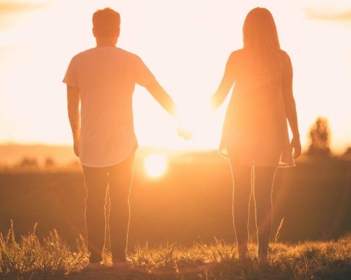 man and woman holding hands white facing sunset