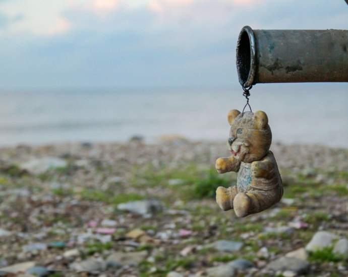 a teddy bear hanging from a pipe near a body of water