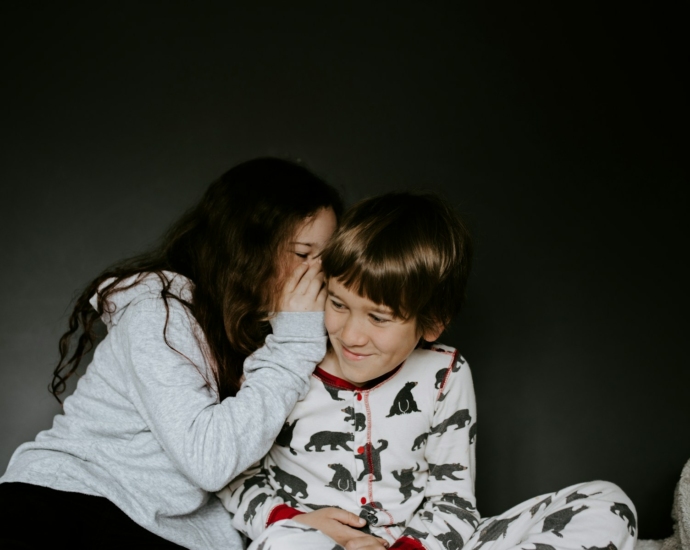 girl in gray jacket whispering on boy's right ear