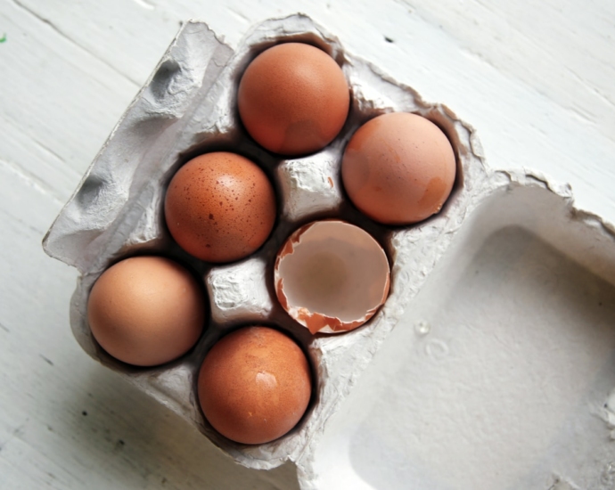 five whole eggs and one empty half-open egg inside open egg tray