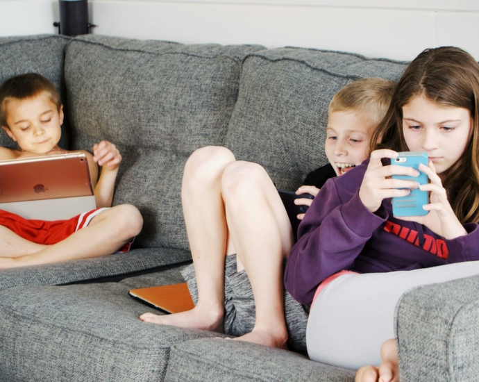 Positive barefoot children in casual wear resting together on cozy couch and browsing tablets and smartphones