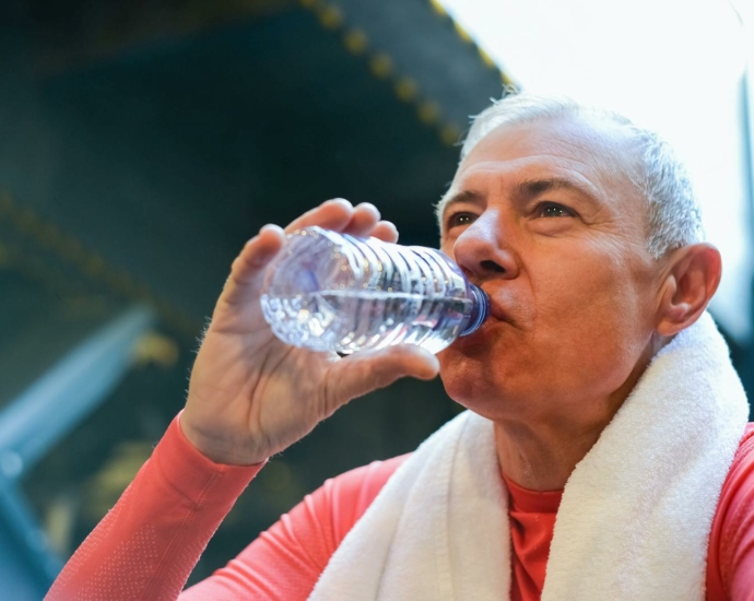 Elderly Man in Red Shirt Drinking Water from a Plastic Bottle