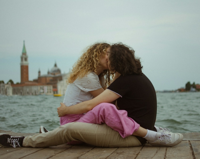 A man and a woman sitting on a pier kissing