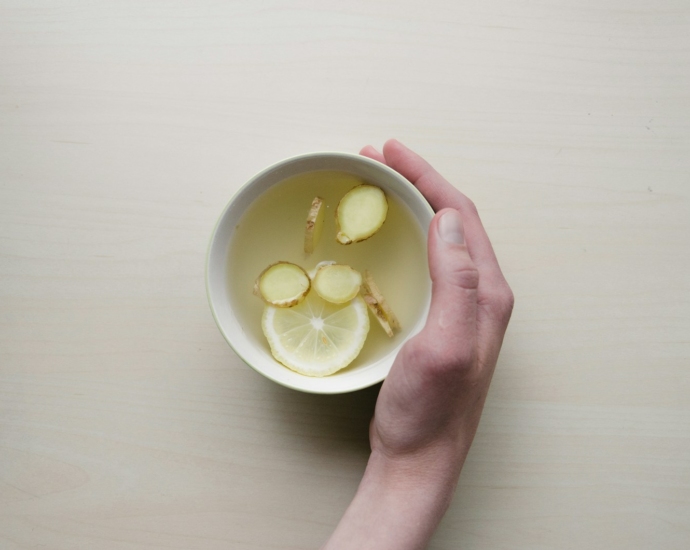 person holding white bowl with sliced lime and ginger inside