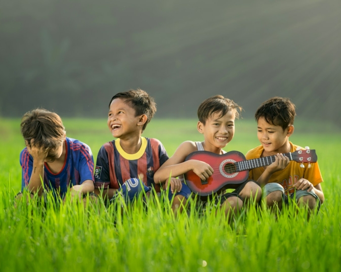 four boys laughing and sitting on grass during daytime