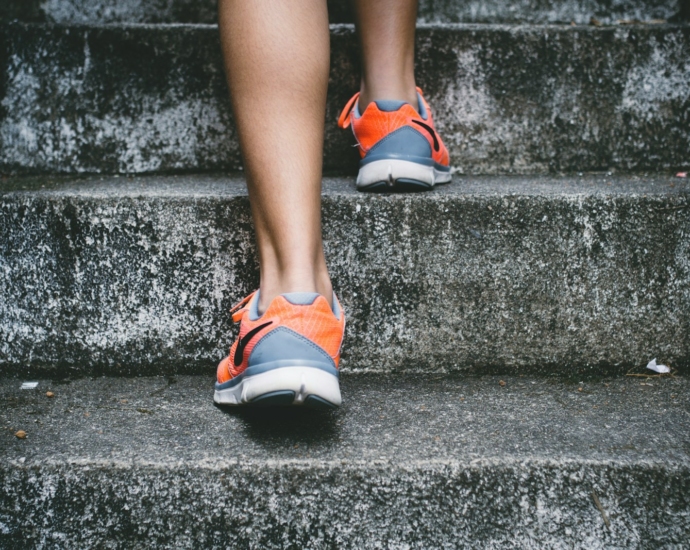 person wearing orange and gray Nike shoes walking on gray concrete stairs