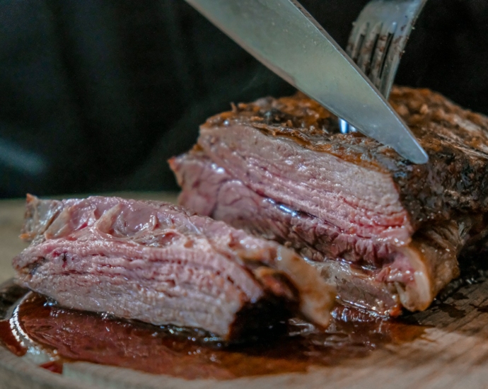 person slicing juicy medium rare meat on top of brown wooden cutting board