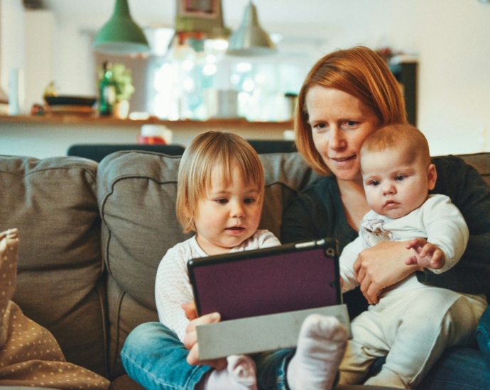 two babies and woman sitting on sofa while holding baby and watching on tablet