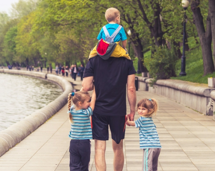 man in black t-shirt and brown shorts holding girl in blue and black jacket walking