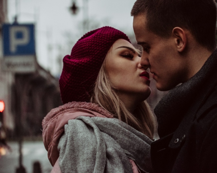 man and woman standing while kissing beside street signage