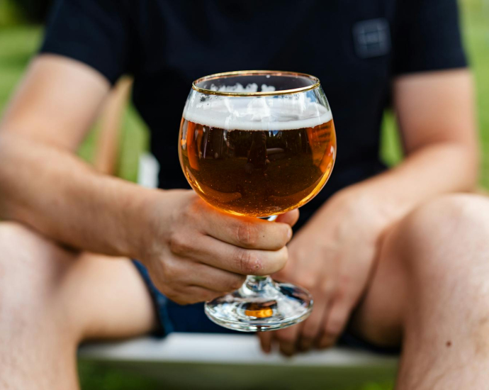 A man holding a glass of beer in an outdoor setting during the day.