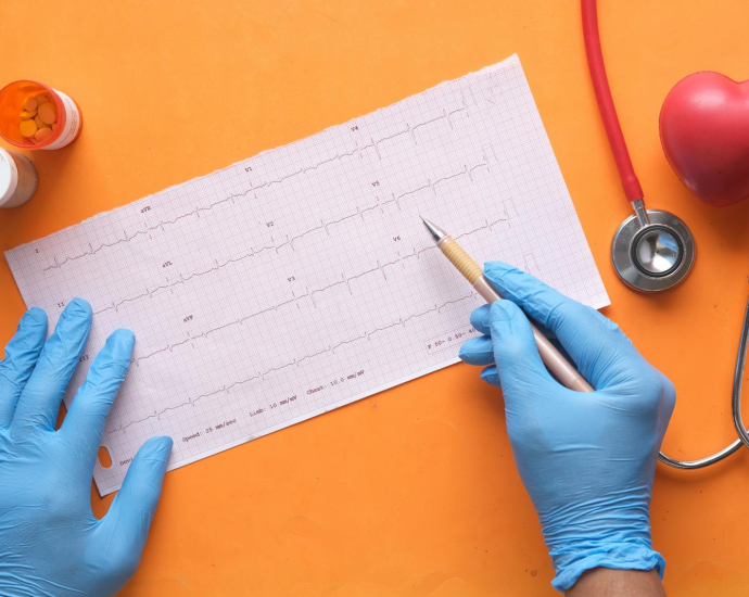 Hands with gloves analyzing an electrocardiogram on an orange background with stethoscope and pills.