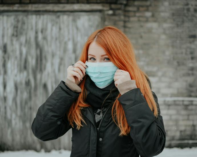 woman in black jacket covering her face with white ceramic mug