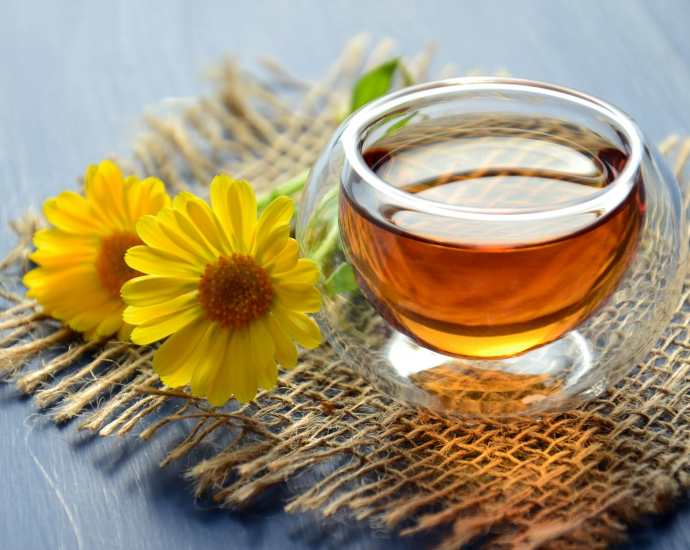 Glass cup of herbal tea with yellow flowers on a textured background.