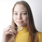 Portrait of a smiling young woman in a yellow sweater holding a biscuit.