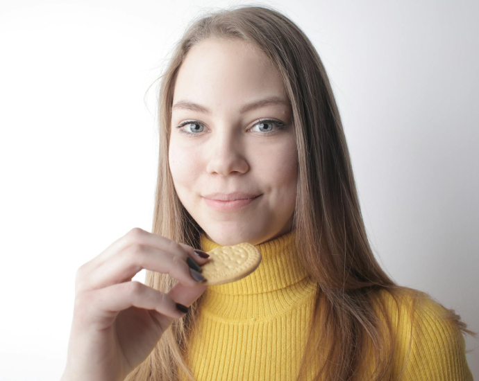 Portrait of a smiling young woman in a yellow sweater holding a biscuit.