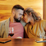 A couple shares an intimate moment with wine glasses at a cozy restaurant setting.