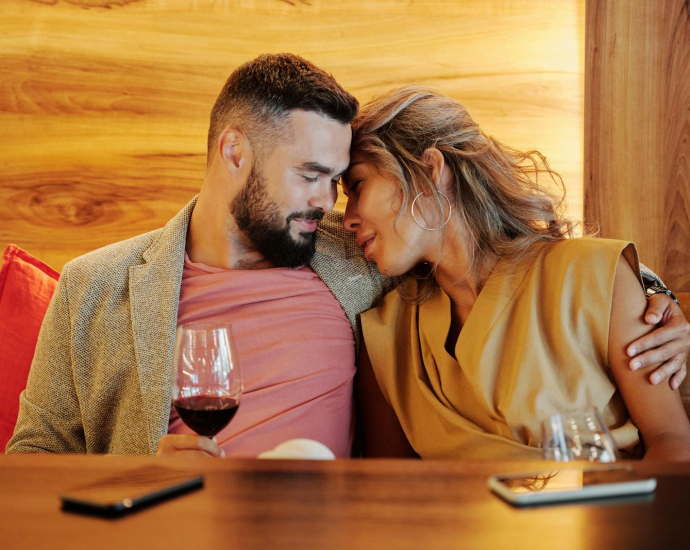 A couple shares an intimate moment with wine glasses at a cozy restaurant setting.