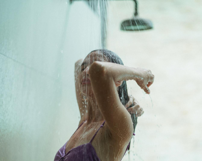 A young woman in a swimsuit enjoys an outdoor shower, capturing a moment of relaxation and tranquility.