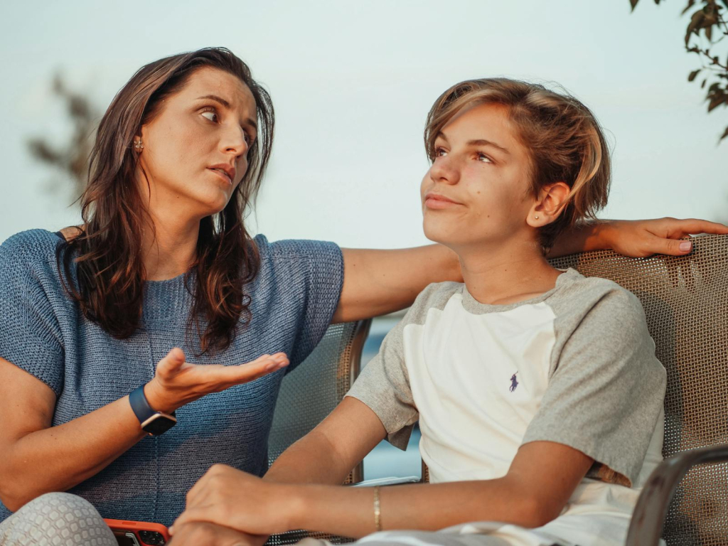 A mother and her teenage son engage in a conversation sitting outside, expressing familial warmth and connection.