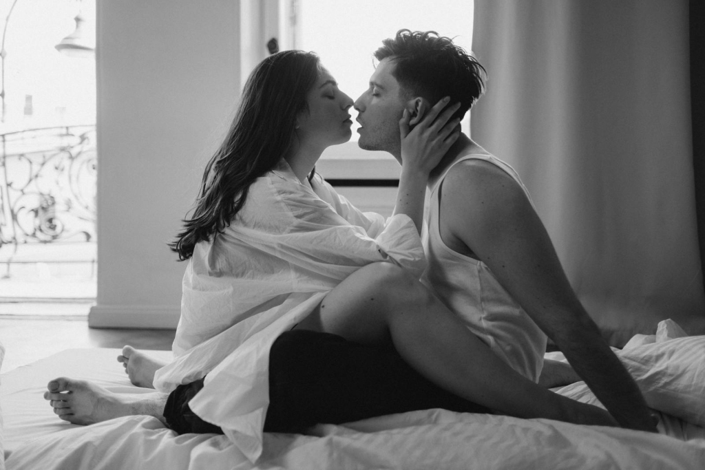 Monochrome image of a romantic couple kissing on a bed in an intimate setting. Captures love and passion.