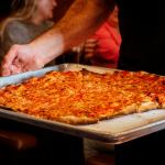 a person holding a tray with a pizza on it