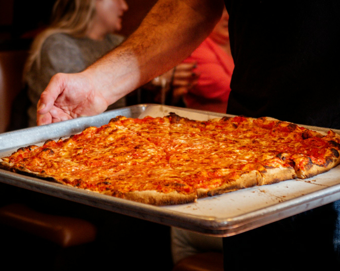 a person holding a tray with a pizza on it