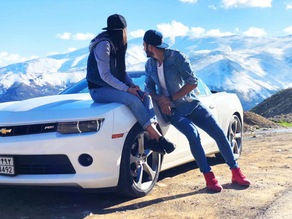 A young couple enjoys a scenic mountainous view while seated on a sports car.