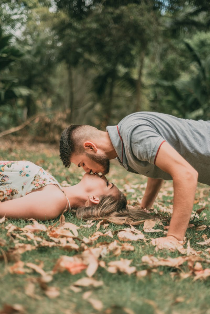 Young couple kissing on grass surrounded by fallen autumn leaves.