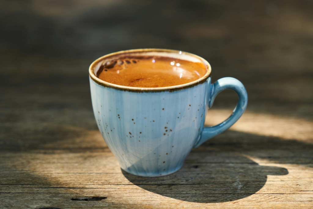 Close-up of a Turkish coffee cup on a rustic wooden table outdoors in warm sunlight.