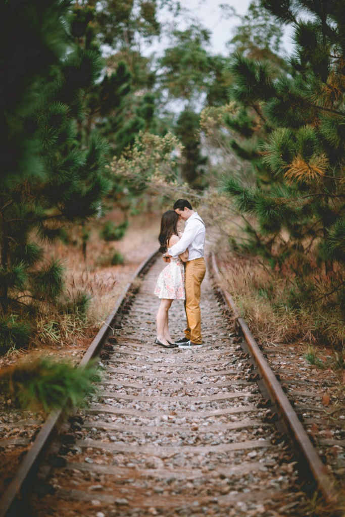 A romantic couple embracing on railway tracks surrounded by nature, depicting love and togetherness.