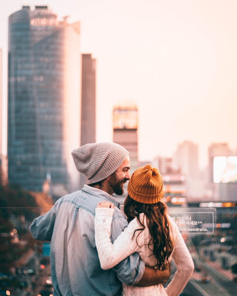 Couple embracing with Seoul skyline backdrop, wearing winter clothing.