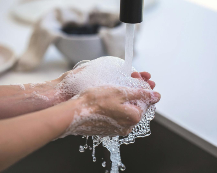 Close-up of hands being washed with foamy soap under a faucet, highlighting hygiene and cleanliness.