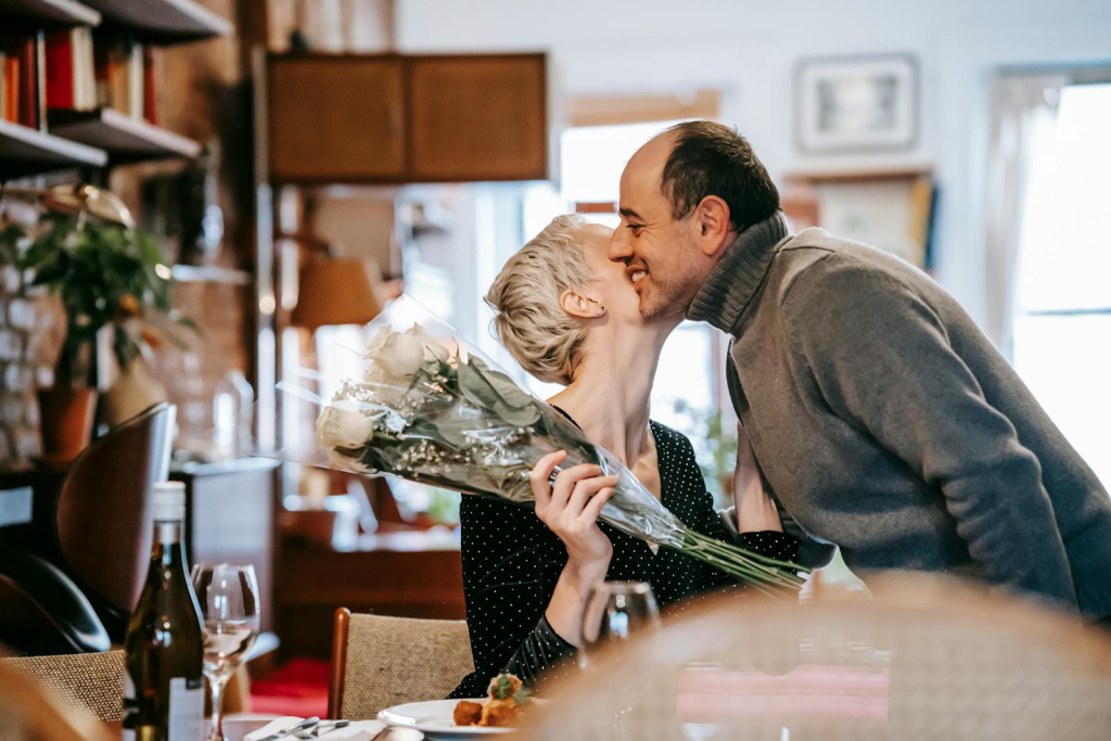 A couple shares a tender moment with a bouquet in a cozy restaurant setting.