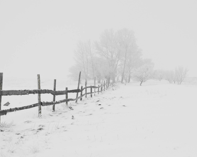 A serene winter scene featuring a rustic wooden fence in a snow-covered landscape.