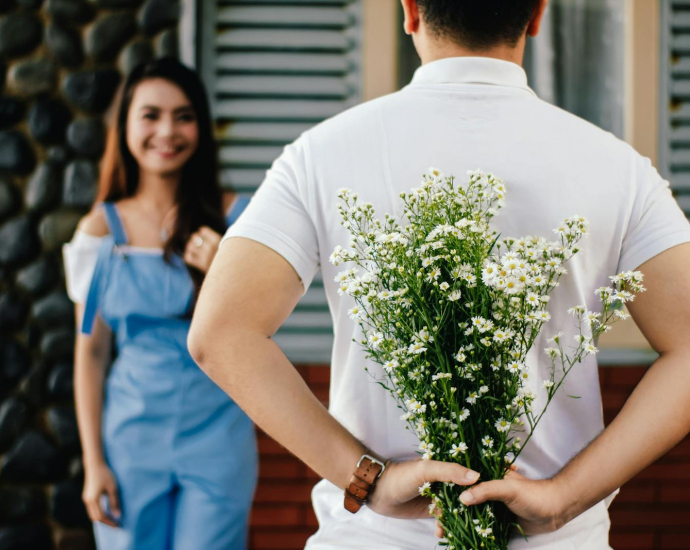 A man surprises his partner with flowers behind his back, symbolizing love and romance.