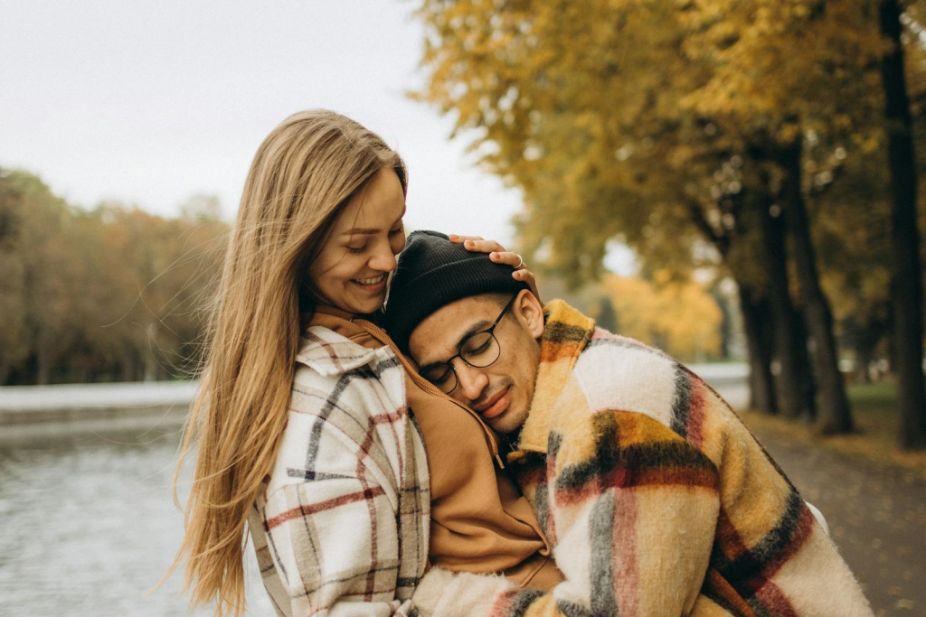 A loving couple embraces by a riverside in an autumn park, showcasing warmth and affection.