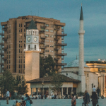 a group of people walking around a plaza with a clock tower in the background